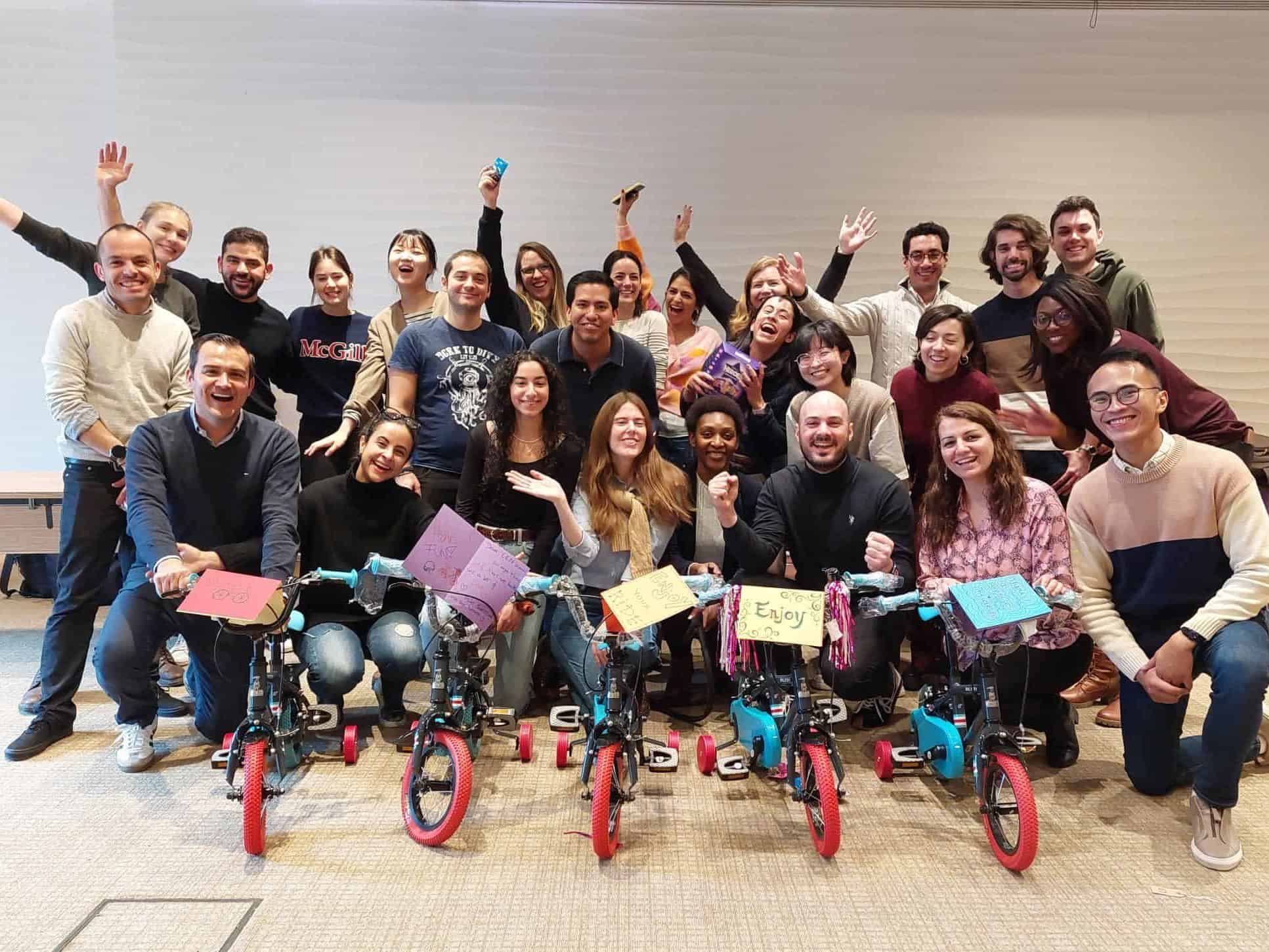 A group photo of colleagues sitting and standing behind bikes they built for charity at a corporate event.