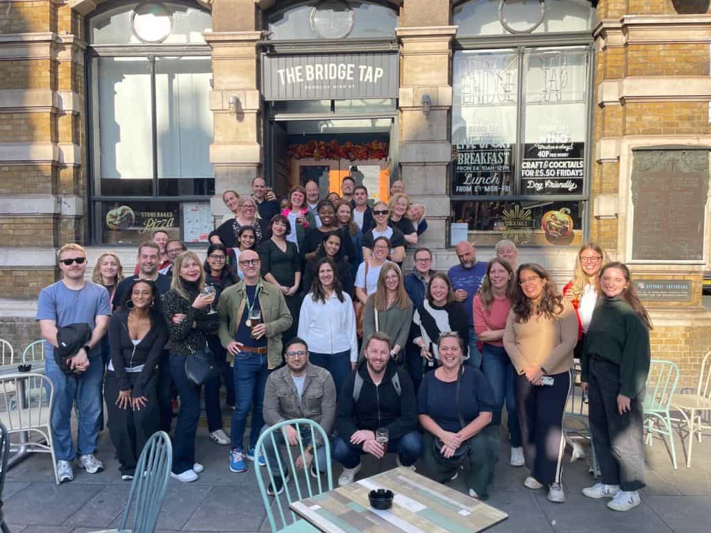 A large group of employees posing happily in a large group. They are gathered outdoors on a sunny day, conveying a cheerful atmosphere.
