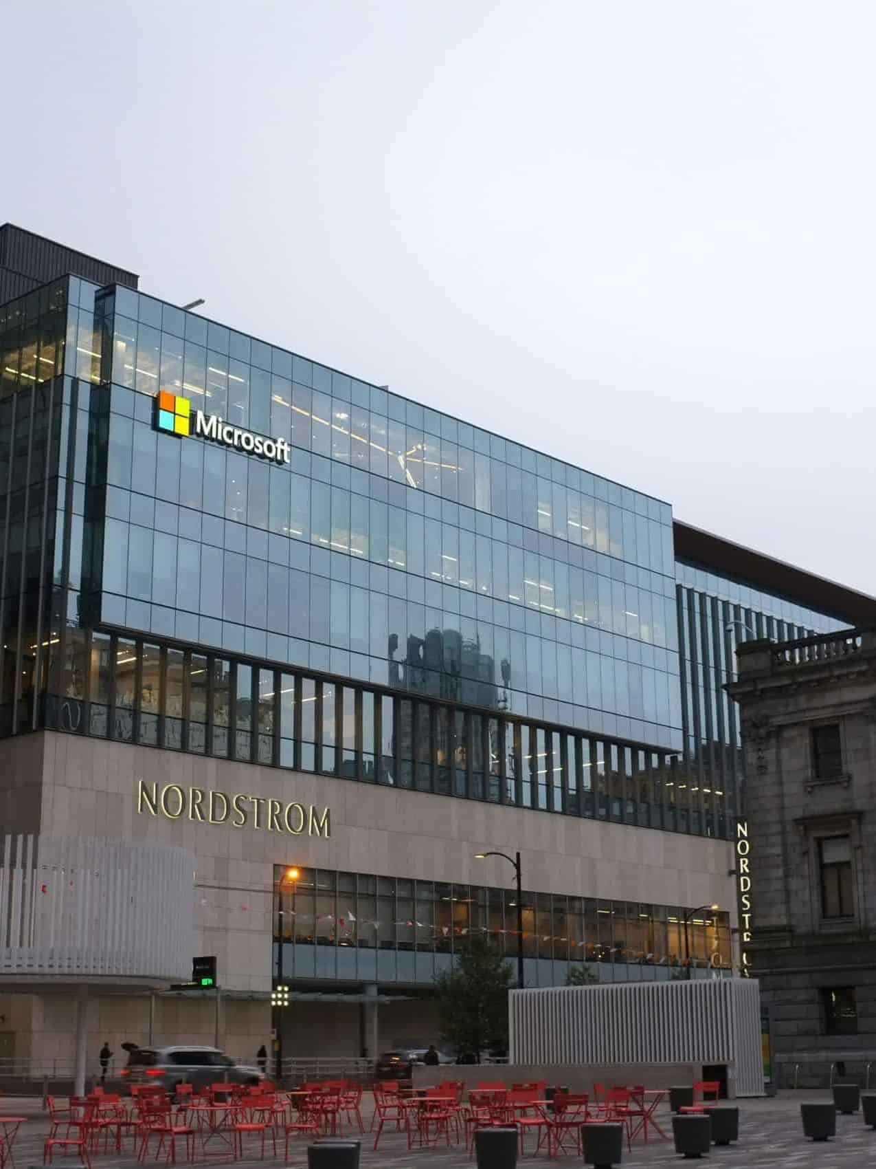 Modern glass buildings under cloudy skies, featuring Microsoft and Nordstrom logos. Red chairs fill the foreground, creating a calm, urban atmosphere.